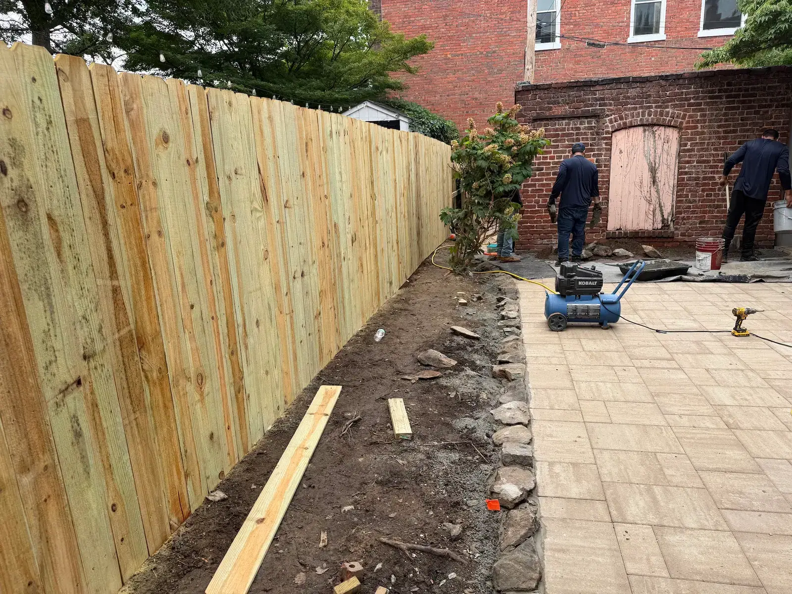Paver installation and planting bed preparation along the fence