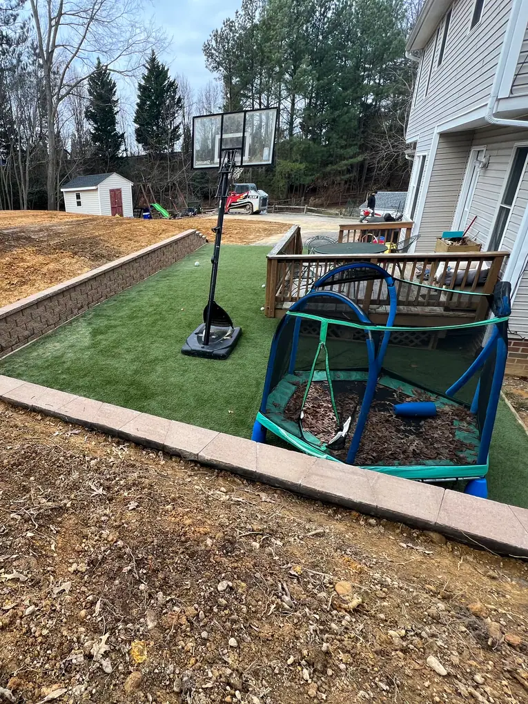 Block retaining wall framing a recessed backyard with artificial lawn during site work