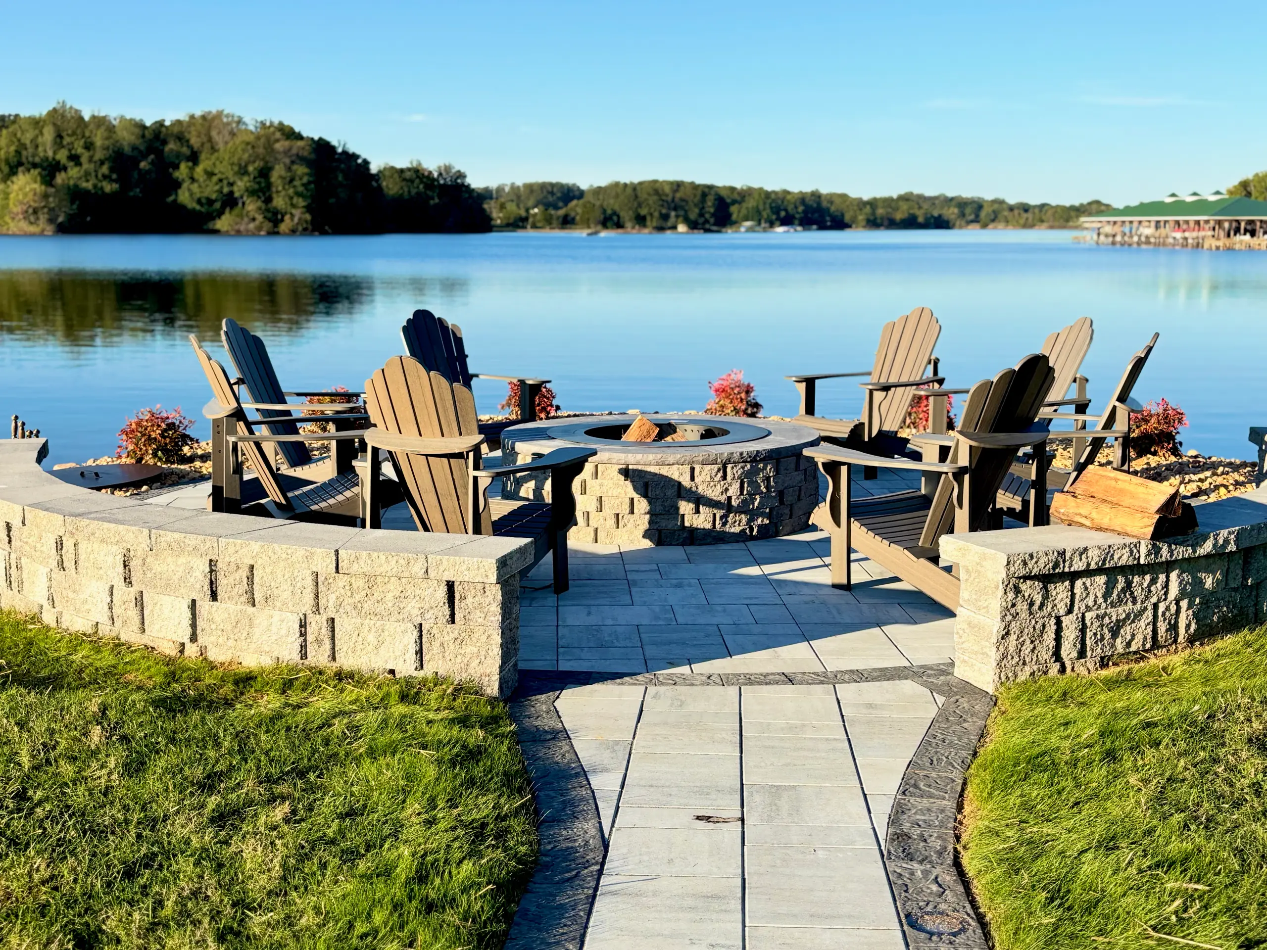 Lakeside stone fire pit with Adirondack chairs, a paver patio and walkway by Willow Landscaping